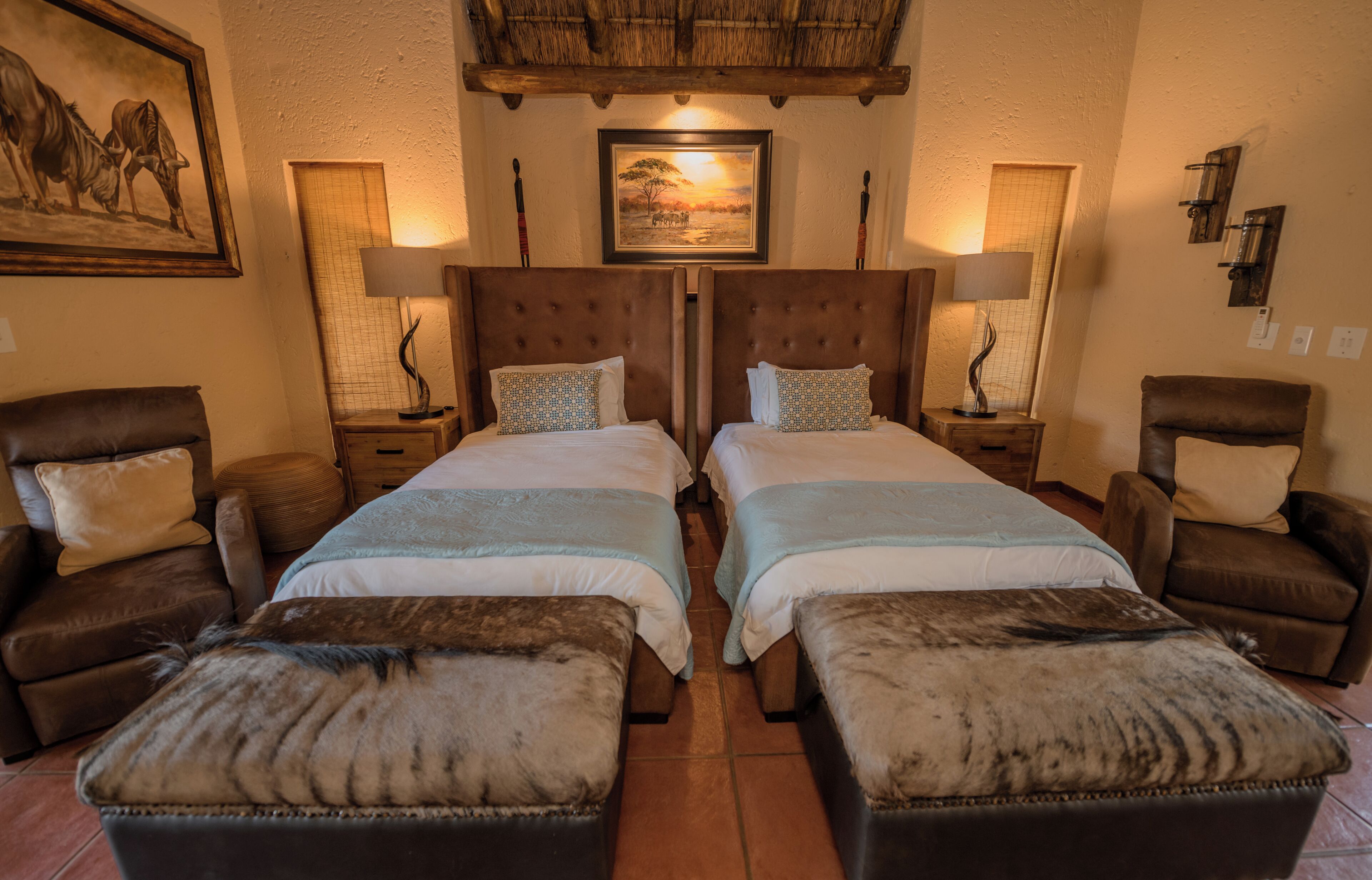 A room with two beds, a large painting, and a chandelier.