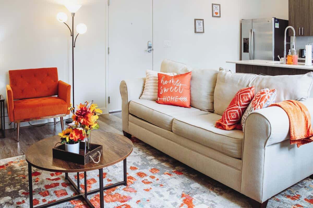 A living room with a sofa, armchair, coffee table, and a kitchen area in the background.