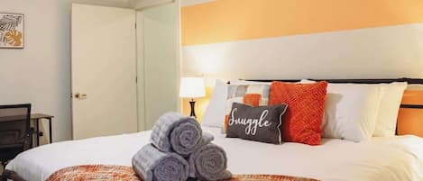 Habitación de hotel con cama, almohada que dice 'Snooze', toalla enrollada y manta.