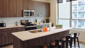 Une cuisine moderne avec des meubles de couleur bois foncé, des appareils électroménagers en acier inoxydable et une grande fenêtre offrant une vue sur l’extérieur du bâtiment.