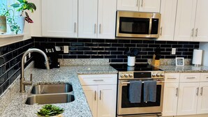 Uma cozinha moderna com armários brancos, uma pia de aço inoxidável, micro-ondas e forno.