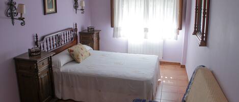 Un dormitorio con cama, mesita de noche, cómoda, ventana con cortinas y espejo en la pared.
