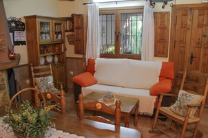 Una habitación acogedora con un sofá de madera, un sillón mecedora, un armario de madera y una ventana con cortinas.