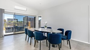 A modern dining area with a round table, six blue chairs, and a potted orchid.