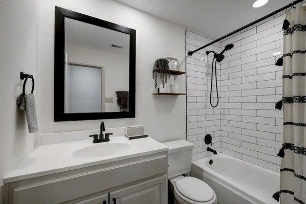 A modern bathroom with a white sink, mirror, and toilet, a shower with a black hose, and a white tiled wall.