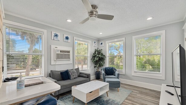 A modern living room with a ceiling fan, a dining area with a table and chairs, and large windows with blinds.
