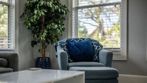 A room with a grey armchair, a large potted plant, and a window with blinds.