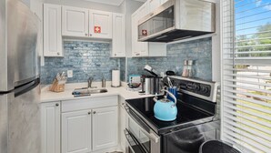 A modern kitchen with white cabinets, a stainless steel refrigerator, a microwave, and a black stove.
