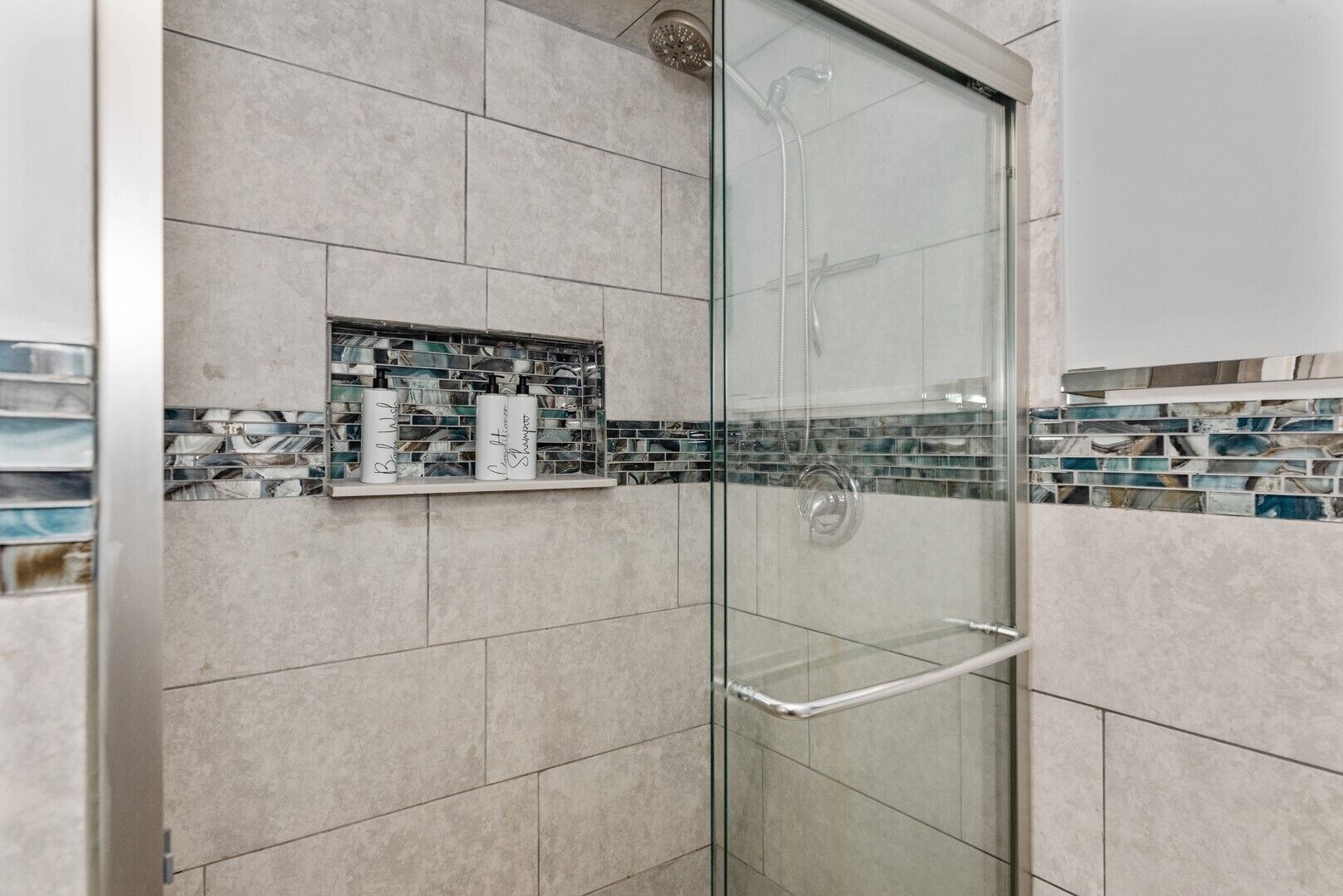 A glass-enclosed shower with a shelf holding toiletries.