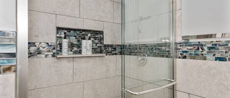 A glass-enclosed shower with a shelf holding toiletries.