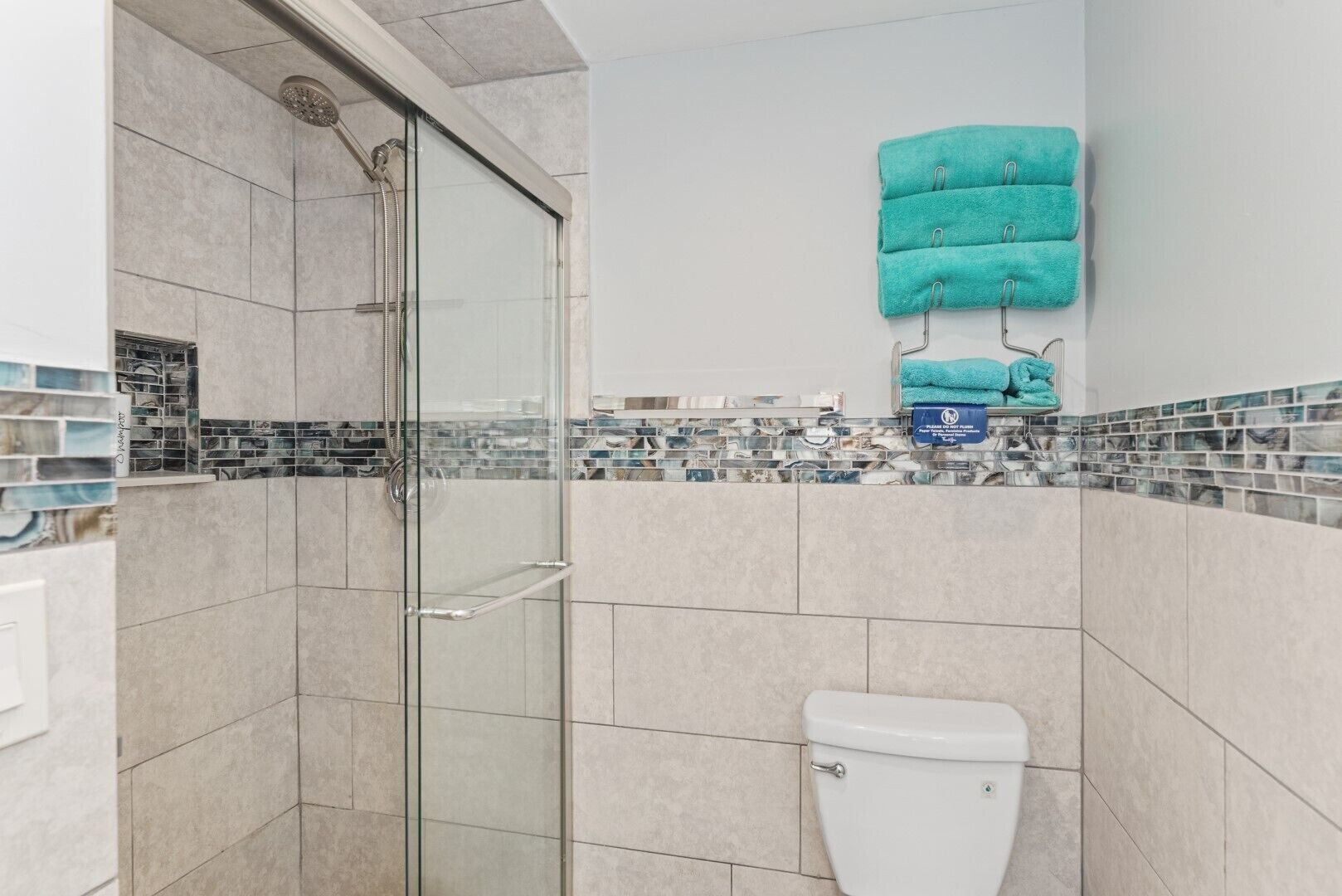 Un baño moderno con ducha envuelta en vidrio, inodoro y salpicadero de azulejos.