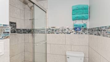 Un baño moderno con ducha envuelta en vidrio, inodoro y salpicadero de azulejos.