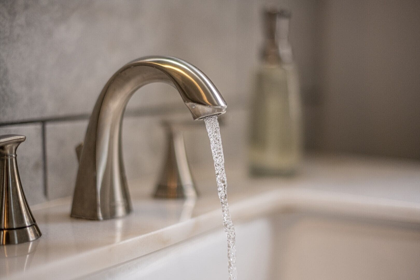 A modern bathroom with a stainless steel faucet and a clear glass bottle in the background.