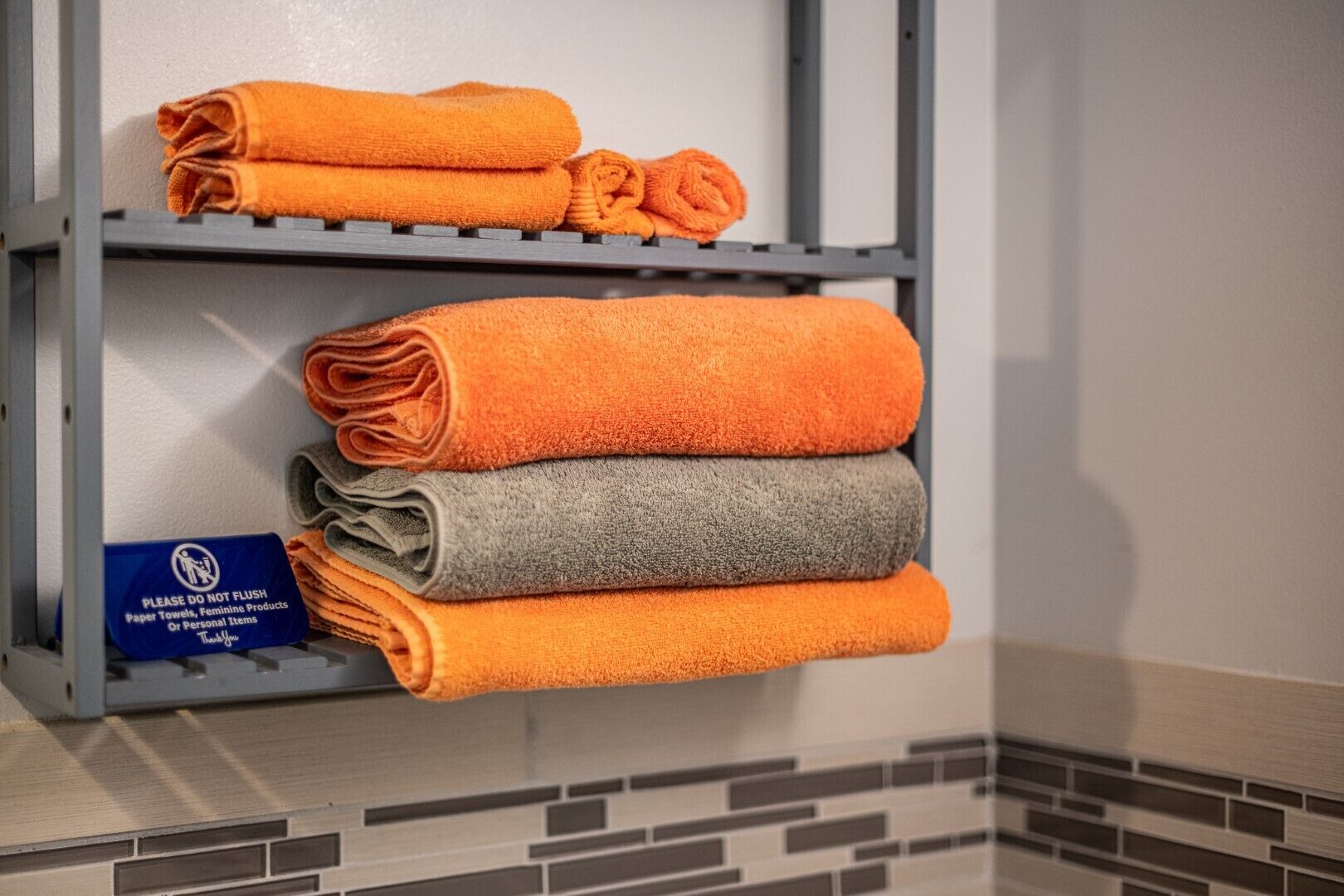 A stack of towels in an orange and gray color scheme on a metal shelf in a hotel room.