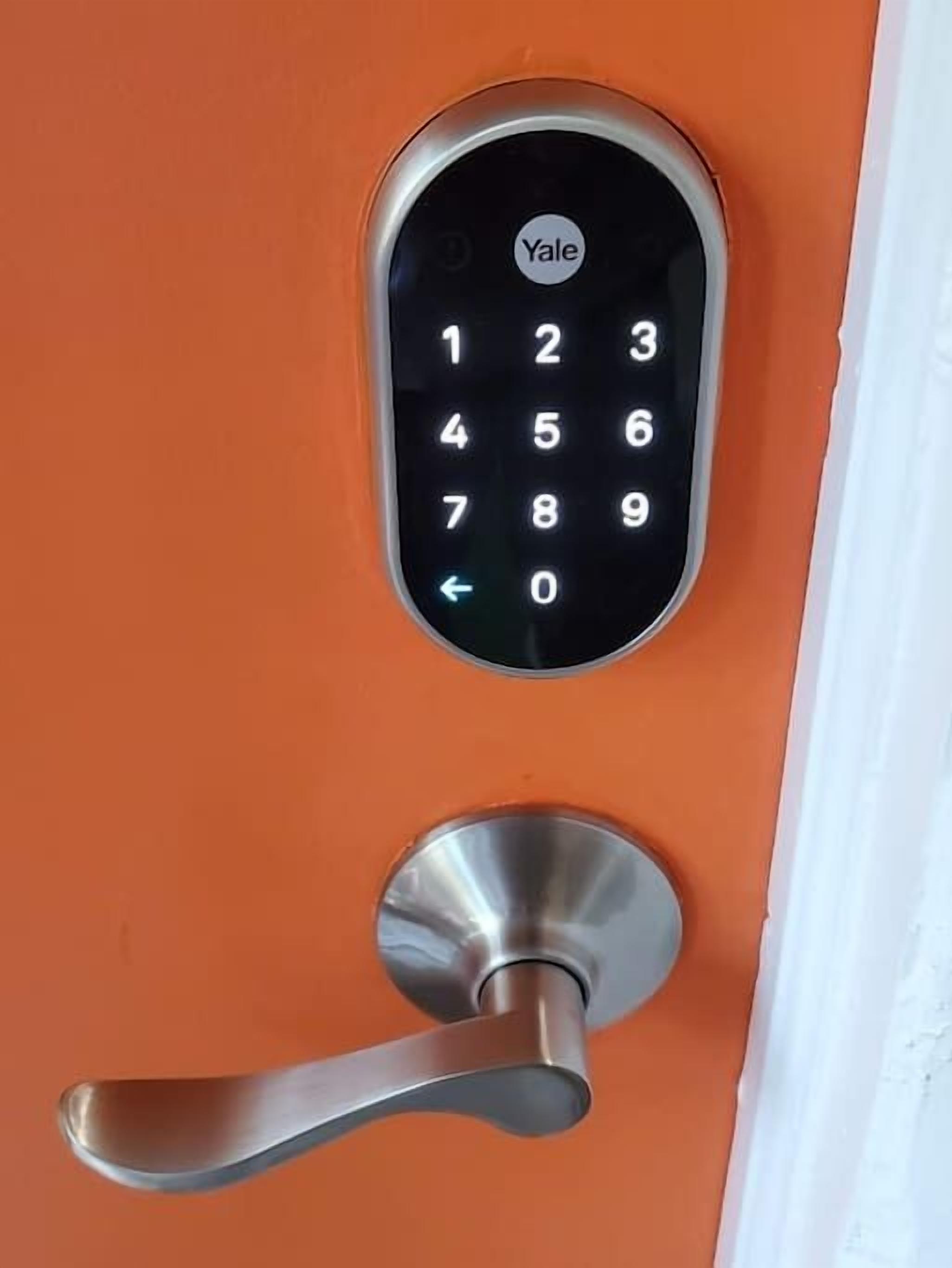 Une serrure électronique de la marque Yale sur une porte orange dotée d’une poignée de porte argentée.