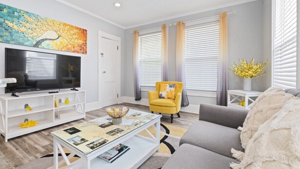 A modern living room with a flat-screen TV, a yellow armchair, a grey sofa, and a coffee table with magazines.
