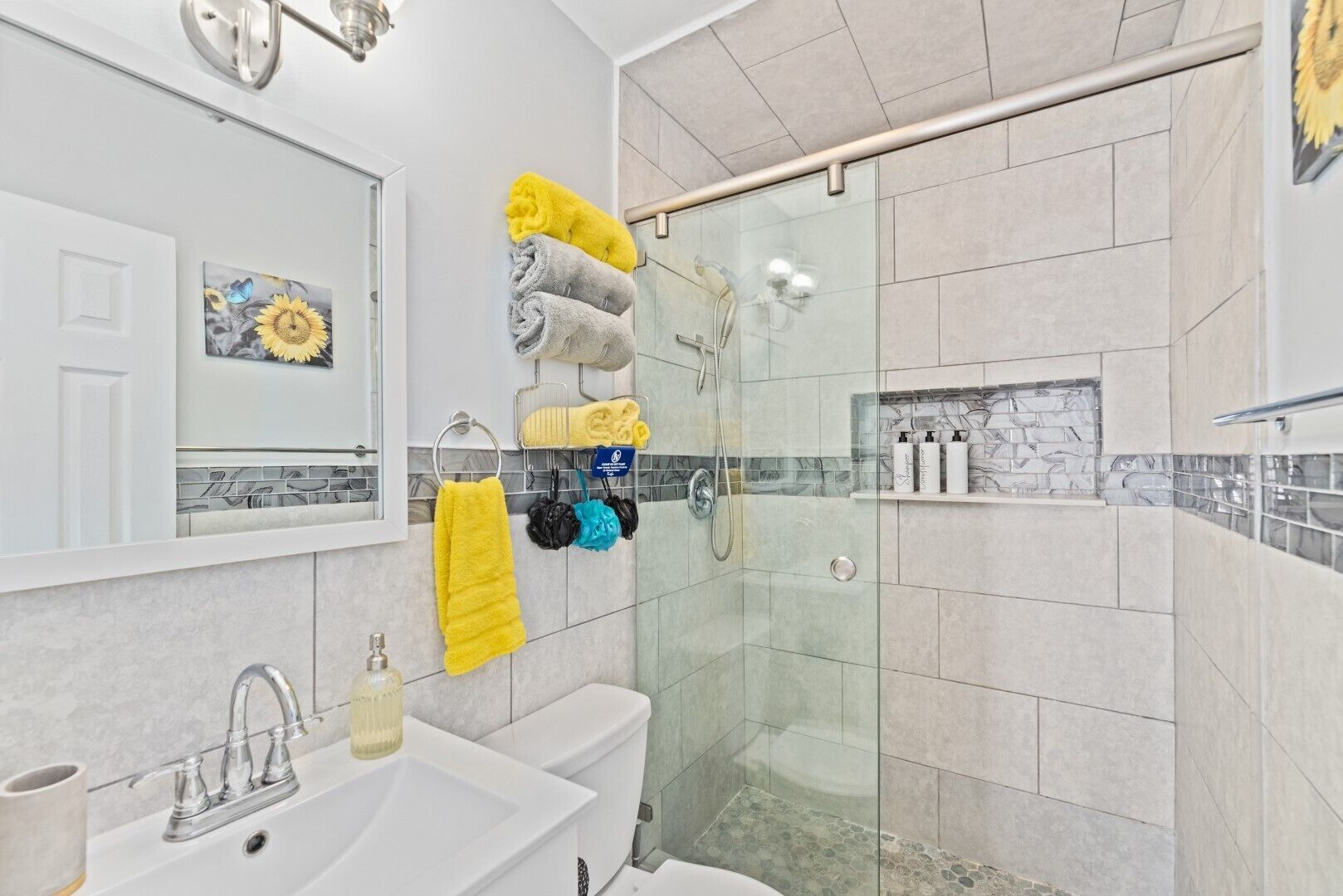 Un baño moderno con cabina de ducha de vidrio, lavabo con espejo y toallero con varias toallas.