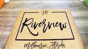 A staircase leading to a wooden door with a doormat that reads "The Riverview Melbourne, Florida".