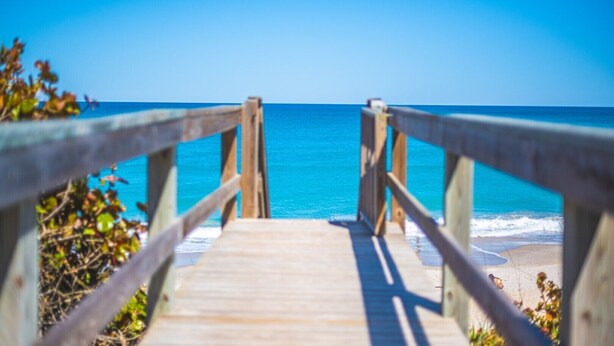 A wooden pier leading to a beach with clear blue water. - Tranquility Octopus Suite - Oceanfront Paradise! (Melbourne Beach)