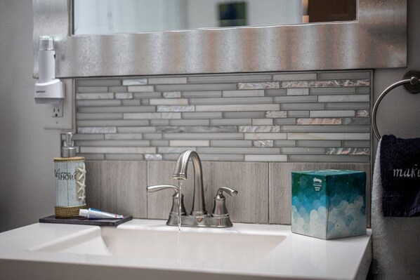 A bathroom with a white sink, a modern faucet, and a tiled backsplash.