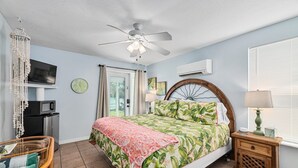 A bedroom with a bed, a ceiling fan, a TV, a clock, a microwave, a refrigerator, a wooden nightstand, and a window with blinds. - Crane Creek Inn Mangrove Suite: Waterfront Pool! (Melbourne)