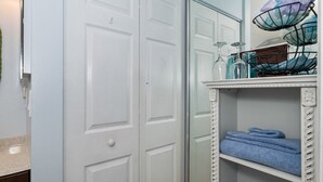 A bathroom with white doors, a mirror, a shelf with towels, and a metal rack with glassware. - Crane Creek Inn Mangrove Suite: Waterfront Pool! (Melbourne)