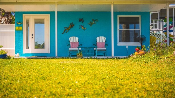 A house with a blue exterior, two white chairs, and a small table. - Crane Creek Inn Mangrove Suite: Waterfront Pool! (Melbourne)