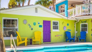 A colorful building with a pool, featuring a purple door, yellow and blue chairs, and decorative fish and sun motifs. - Crane Creek Inn Dolphin Suite: Waterfront Pool! (Melbourne)