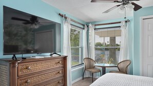 A bedroom with a TV, wooden dresser, two wicker chairs, a small table, and a bed. - Crane Creek Inn Dolphin Suite: Waterfront Pool! (Melbourne)