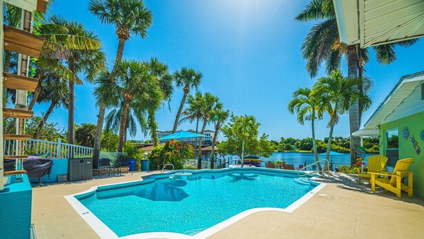 A swimming pool surrounded by palm trees and a beach area with lounge chairs. - Crane Creek Inn Manatee Suite: Waterfront Pool! (Melbourne)