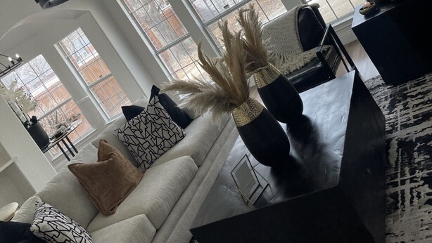 A modern living room with a chandelier, large windows, a sofa, and decorative items.