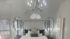 A bedroom with a four-poster bed, a chandelier, and a large window.