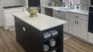 A modern kitchen with white cabinetry, a black island, and a large window.