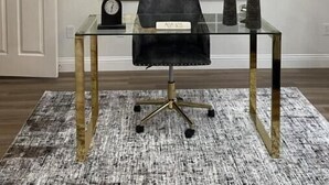 A modern office desk with a glass top, a black office chair, and a decorative chandelier.