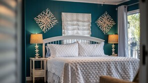 A bedroom with a bed, two bedside tables with lamps, decorative wall art, and a window with curtains.