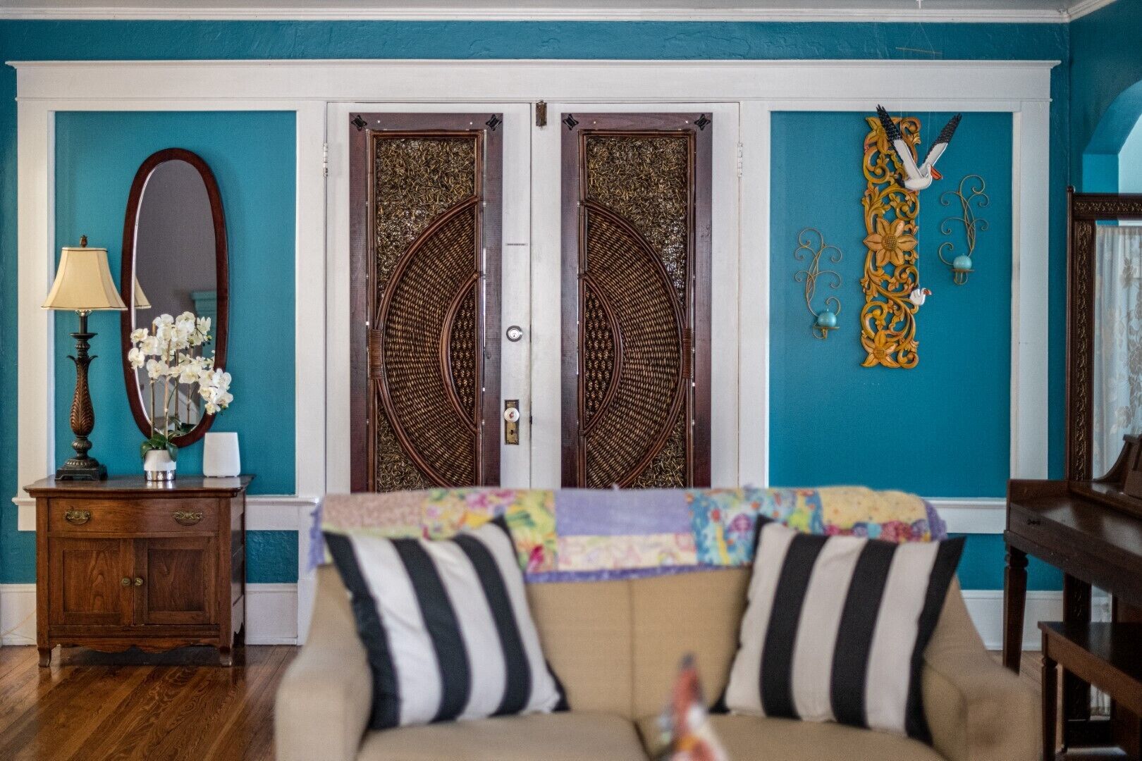 Una habitación con paredes color turquesa, un armario de madera con espejo y lámpara, dos puertas decorativas y un adorno floral en la pared.