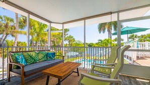 A covered outdoor seating area with a wooden table and chairs, overlooking a pool and palm trees.