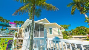 A two-story house with a balcony, surrounded by palm trees and a clear blue sky.