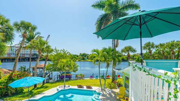 A swimming pool with a view of a body of water, surrounded by palm trees and a white fence.