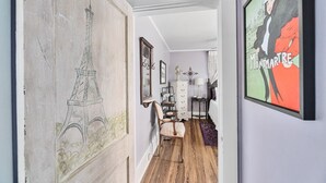 Un pasillo con un dibujo grande de la Torre Eiffel, un tocador blanco y una foto enmarcada de Montmartre.