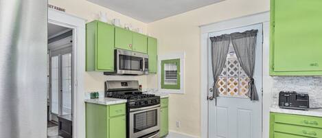 A compact kitchen with green cabinets, a stainless steel refrigerator, a microwave, a stove, and a WestBond toaster.