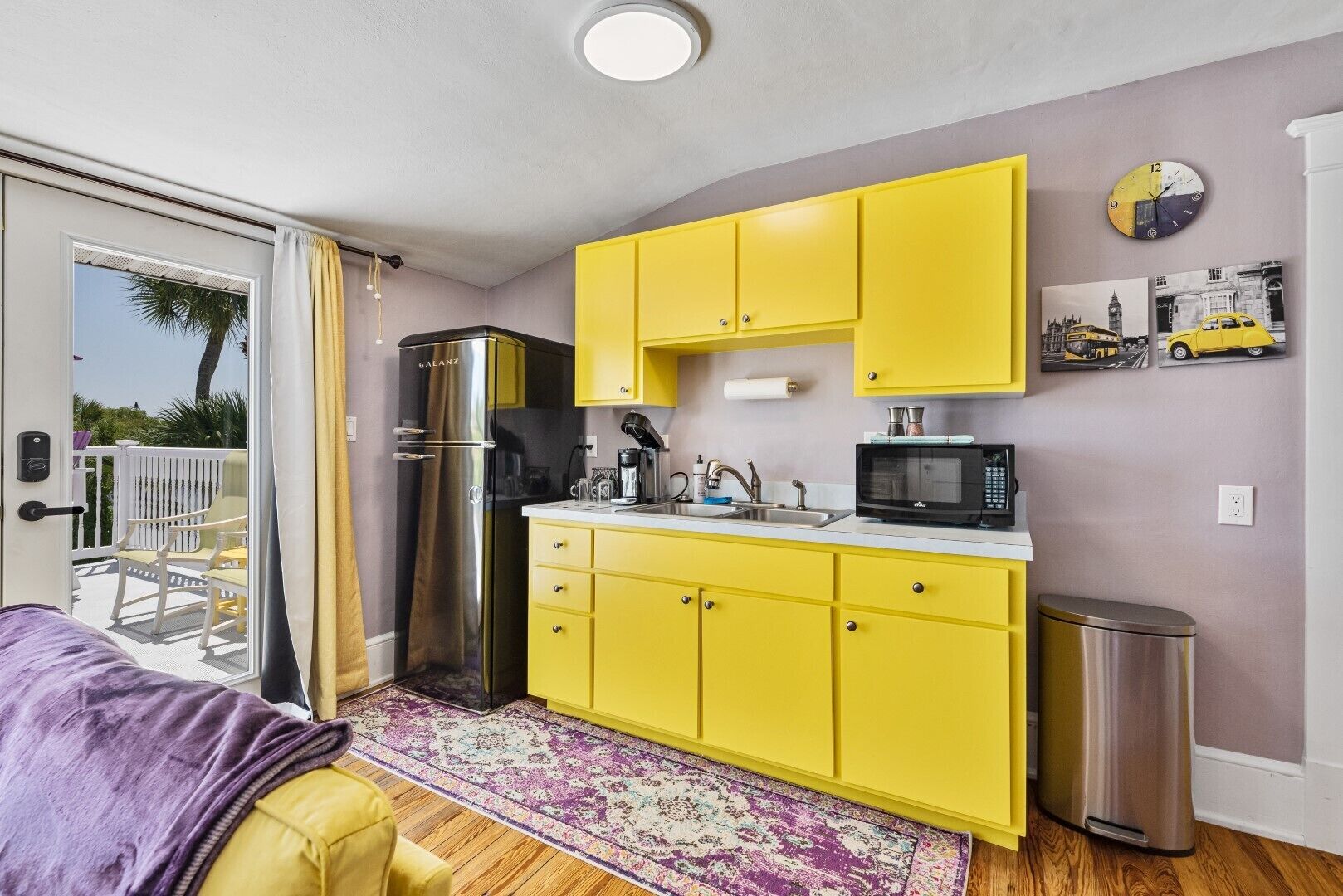 A compact kitchen with yellow cabinets, a stainless steel refrigerator, a microwave, and a sink.