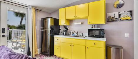 A compact kitchen with yellow cabinets, a stainless steel refrigerator, a microwave, and a sink.