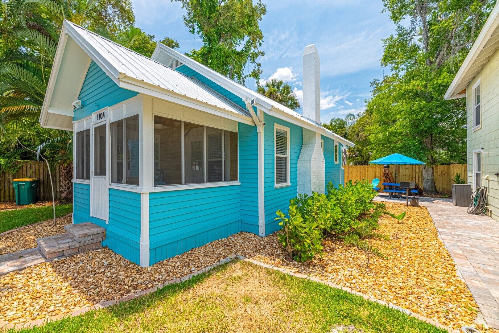 A small, single-story house with a blue exterior and a white roof. It has a front porch with a set of steps leading to the door.