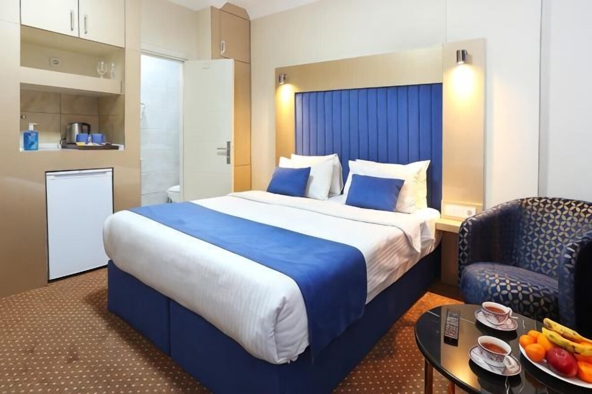 Une chambre d’hôtel avec un lit, une petite kitchenette, une chaise et une table avec des fruits et des tasses.