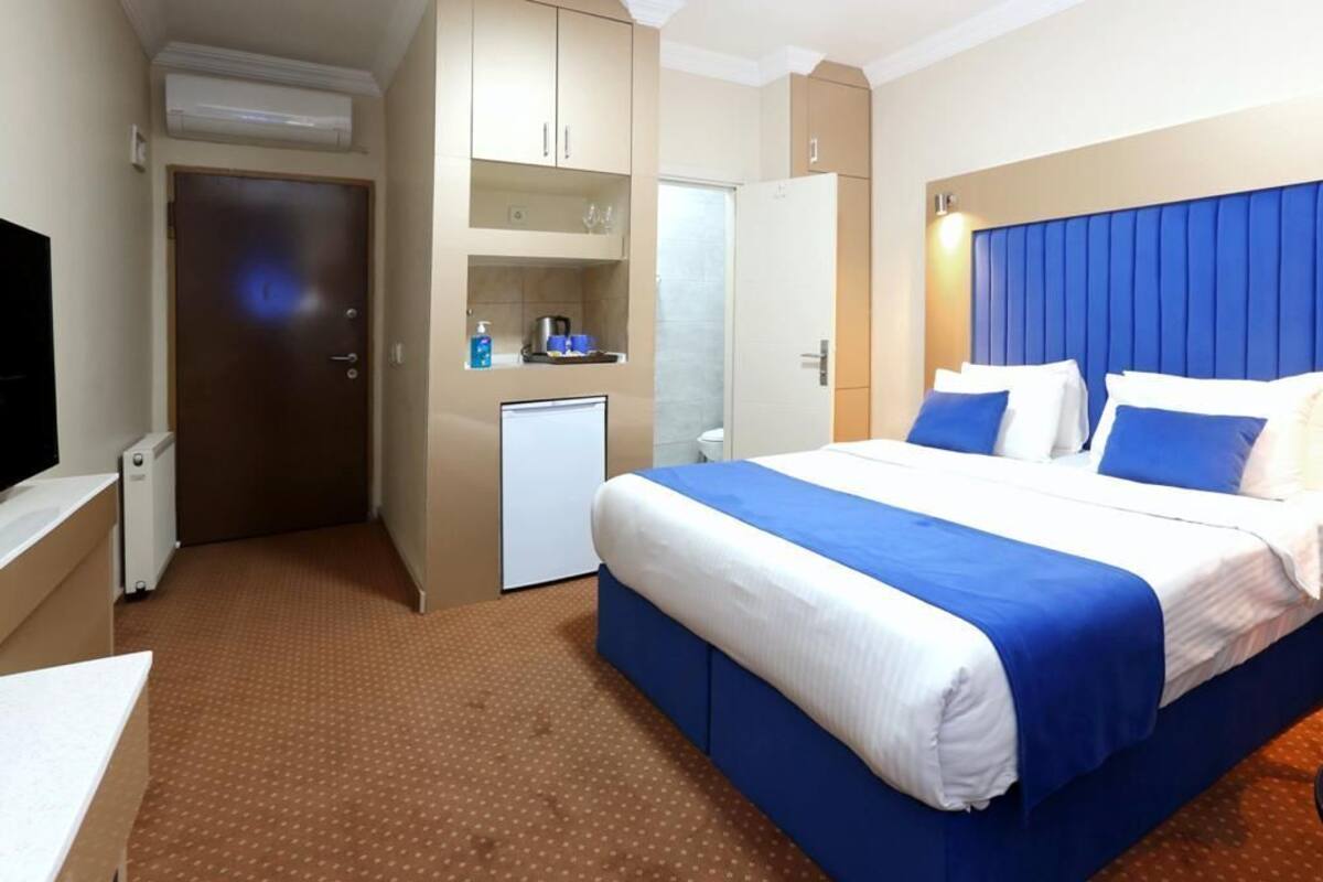 A hotel room with a bed, a desk, a small refrigerator, a TV, and a bathroom.