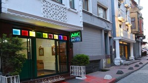 A hotel with a glass facade, a sign reading "ABC HOTEL", and a small garden area with a bench and a potted plant. - Taksim ABC Hotel (Istanbul)