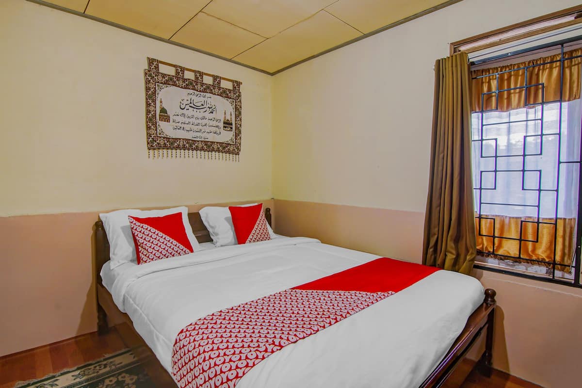 A neatly made bed with a red and white patterned bedspread, a framed certificate on the wall, and a window with curtains.