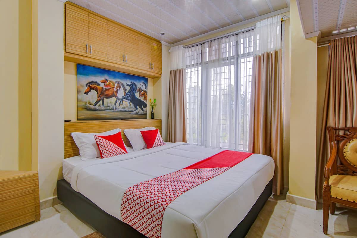A hotel room with a large bed, wooden headboard, a painting of horses, and a window with curtains.