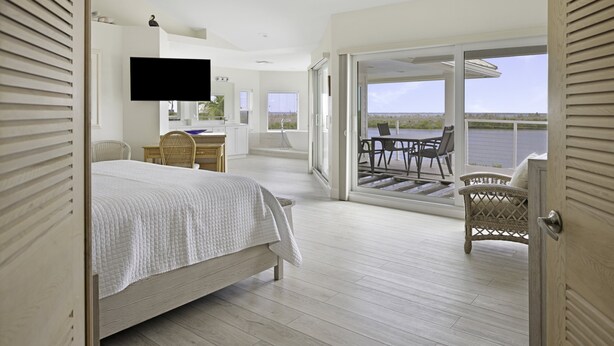 A bedroom with a bed, a desk, a television, and a view of the outdoors.